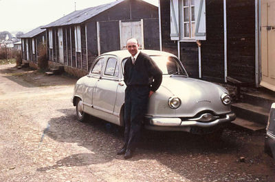 Un habitant de Keredern pause devant sa Dyna Z Panhard. En arrière plan, des baraques de Keredern. Vers 1963.